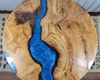 May include: Round wooden table top with a blue resin river flowing through the centre. The wood has a natural grain pattern and the resin has a glossy finish.