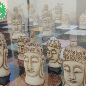 May include: A chess set featuring ivory-colored Buddha head chess pieces on a black and white checkered board. The pieces have detailed facial features and ornate headwear. The image includes a "READY TO SHIP" sticker.
