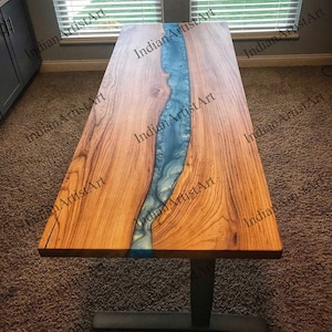 May include: A wooden table with a blue resin river running down the center. The table has a natural wood finish and a black metal base.