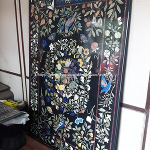 May include: A black marble table top with a floral design inlaid with colorful stones. The design features birds, butterflies, and flowers. The table top is surrounded by a black border.