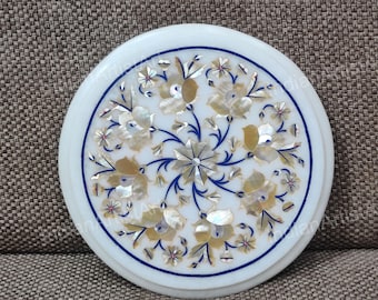 May include: Round white marble coaster with a floral design. The coaster features a detailed inlay of flowers in shades of gold, white, and blue. The design is centered and surrounded by a blue border.