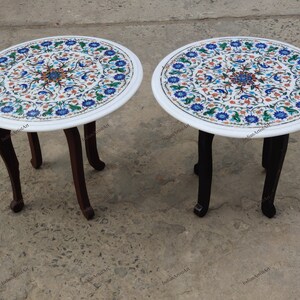 May include: Two round side tables with white marble tops inlaid with a floral pattern in blue, green, and orange. The tables have dark brown, curved legs. Each table is approximately 20 inches in diameter.