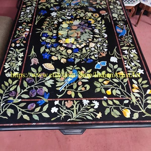 May include: A black marble table top with a floral design inlaid with various coloured stones. The design features birds, flowers, and fruit. The table top is surrounded by a black border.