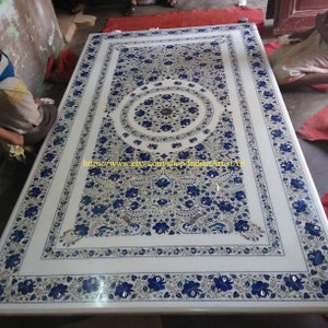 May include: A large, rectangular white marble table with intricate blue floral inlay designs. The table features a central circular pattern and a border of repeating floral motifs. The text "https://www.etsy.com/shop/IndianArtistArt" is visible.