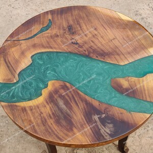 May include: A round wooden table top with a green epoxy river design. The wood is a dark brown colour and the epoxy is a light green colour with swirls.