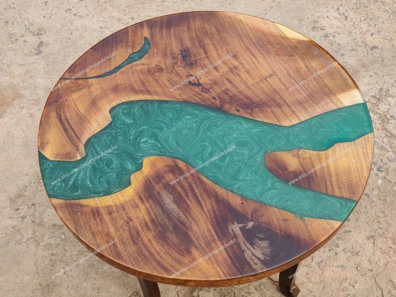 May include: A round wooden table top with a green epoxy river design. The wood is a dark brown colour and the epoxy is a light green colour with swirls.