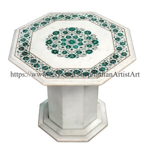 May include: Octagonal white marble table with a green and gold floral inlay design. The table has a single pedestal base.