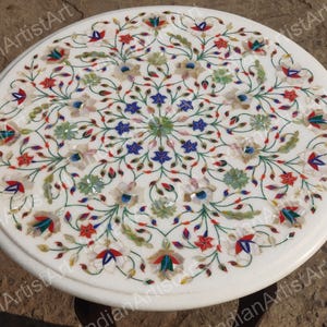 Puede incluir: Tapa de mesa de mármol blanco con un diseño floral incrustado con piedras de colores. El diseño presenta intrincados patrones florales y un motivo central.