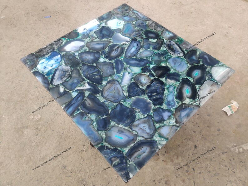 Pu&ograve; includere: Un piano da tavolo quadrato in agata blu e verde. Il piano del tavolo &egrave; composto da molti piccoli pezzi di agata che sono stati tagliati e lucidati. Il piano del tavolo &egrave; posto su una base in metallo.