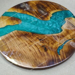 May include: Round wooden table top with a green epoxy resin river design. The wood has a natural brown colour and the resin has a swirling pattern.
