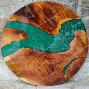 May include: Round wooden table top with a green epoxy resin river design. The wood has a natural brown colour and the resin has a swirling pattern.