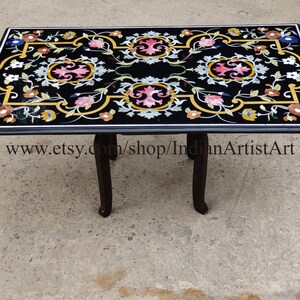 Puede incluir: Mesa rectangular de mármol negro con incrustaciones florales. La mesa tiene un marco y patas de madera oscura. La tapa de la mesa está adornada con coloridos diseños florales en rosa, azul, amarillo y blanco. La URL de la tienda Etsy es visible.