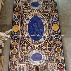 May include: A large, rectangular table top made of inlaid stone. The table top features a complex geometric pattern with a large oval in the center. The oval is filled with a blue stone, surrounded by a border of smaller stones in various colors. The table top is surrounded by a border of smaller stones in various colors.