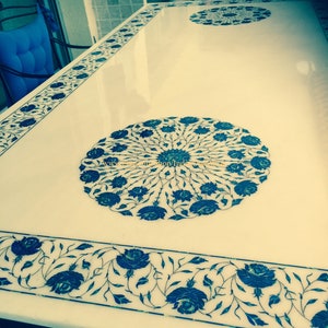 May include: A white marble table top with intricate blue floral designs inlaid into the surface. The table top is polished and reflects light.