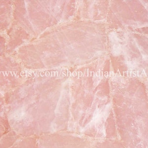 May include: A close-up of a pink rose quartz slab with a natural, irregular, and textured surface. The slab is made up of many smaller pieces of rose quartz that have been joined together.