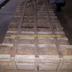 May include: A wooden crate filled with wood shavings, used for packing and shipping fragile items. The crate is made of natural wood and has a rustic appearance. The text "https://www.etsy.com/shop/IndianArtistArt" is printed on the crate.