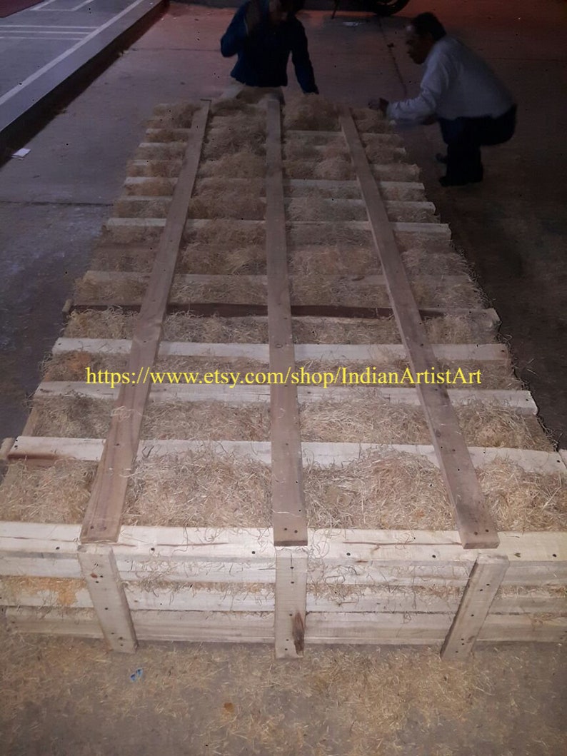 May include: A wooden crate filled with wood shavings, used for packing and shipping fragile items. The crate is made of natural wood and has a rustic appearance. The text "https://www.etsy.com/shop/IndianArtistArt" is printed on the crate.
