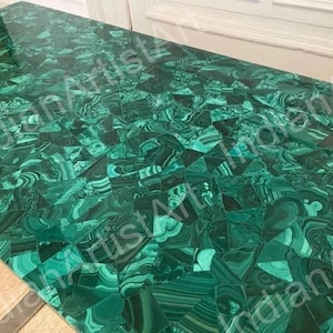 Op de afbeelding: Een groene malachiet tafelblad met een geometrisch patroon. Het tafelblad is gemaakt van veel kleine stukjes malachiet die zijn gesneden en gepolijst om een glad oppervlak te creëren.