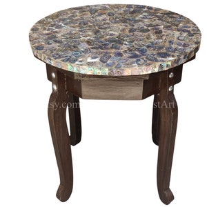 Könnte beinhalten: Ein runder Beistelltisch mit einem dunklen Holzsockel und einer Tischplatte aus irisierenden Perlmutt-Fliesen. Der Tisch hat eine Schublade und drei Beine.