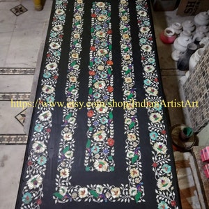 Könnte beinhalten: Eine schwarze Marmortischplatte mit aufwendigen floralen Designs, die mit Perlmutt und anderen bunten Steinen eingelegt sind. Die Tischplatte ist von einem Rand mit dem gleichen Design umgeben.