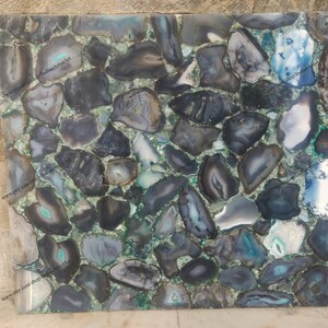 Pu&ograve; includere: Primo piano di una superficie decorativa realizzata con molti piccoli pezzi di agata di forma irregolare. L'agata &egrave; una miscela di colori nero, grigio e verde. La superficie &egrave; liscia e lucida.