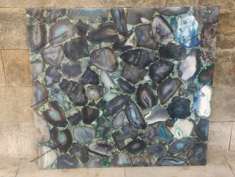 Pu&ograve; includere: Primo piano di una superficie decorativa realizzata con molti piccoli pezzi di agata di forma irregolare. L'agata &egrave; una miscela di colori nero, grigio e verde. La superficie &egrave; liscia e lucida.