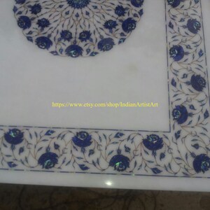 May include: White marble table top with a blue and white floral design. The design features intricate details and is inlaid with lapis lazuli. The table top is surrounded by a border of the same design.