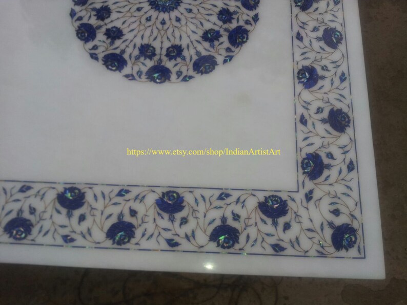 May include: White marble table top with a blue and white floral design. The design features intricate details and is inlaid with lapis lazuli. The table top is surrounded by a border of the same design.