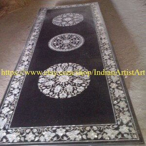 May include: A black marble table top with intricate floral designs inlaid with mother of pearl. The table top has a black border with a floral design.