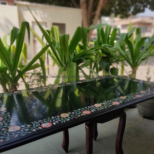 May include: A black marble table with a floral inlay design. The table has a glossy finish and is supported by four legs.