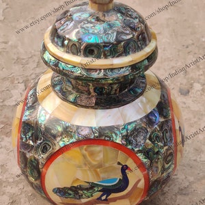 Op de afbeelding: Een decoratieve, ronde, dekselpot gemaakt van ingelegd parelmoer met een pauwenmotief. De pot heeft een rode en oranje rand rond het pauwenmotief.