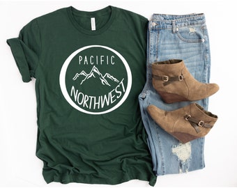 Może przedstawiać: Zielony t-shirt z białym kołem graficznym z tekstem "PACIFIC NORTHWEST" i stylizowanym pasmem górskim.