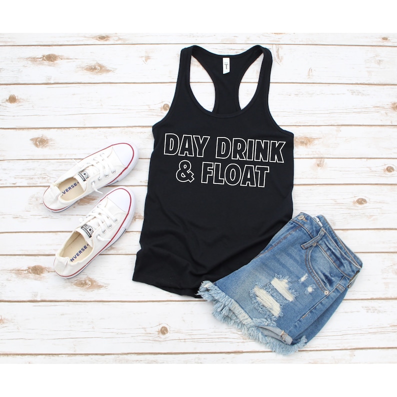 May include: Black tank top with white text that reads "DAY DRINK & FLOAT". The tank top is paired with denim shorts and white sneakers.