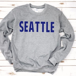May include: A grey sweatshirt with the word "SEATTLE" printed in blue on the front.
