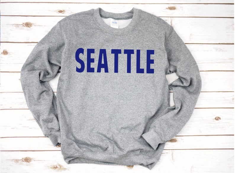 May include: A grey sweatshirt with the word "SEATTLE" printed in blue on the front.