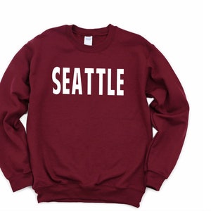 May include: A maroon sweatshirt with the word "SEATTLE" printed in white on the front.
