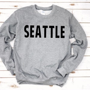 May include: A grey sweatshirt with the word "SEATTLE" printed in black on the front.