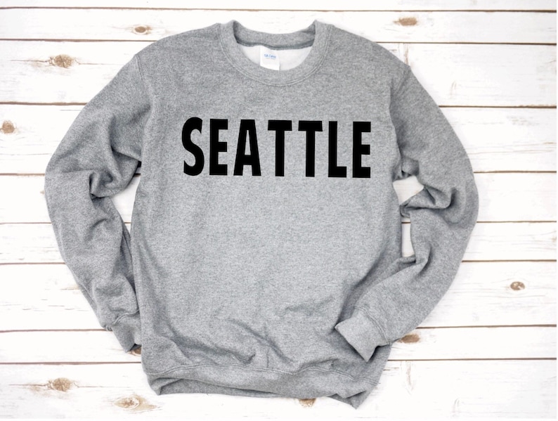 May include: A grey sweatshirt with the word "SEATTLE" printed in black on the front.