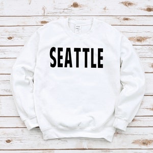 May include: White sweatshirt with black text that reads "SEATTLE".