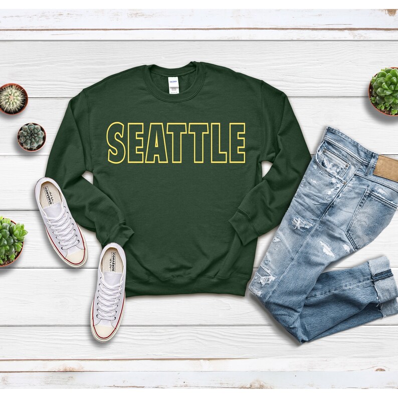 Peut inclure: Un sweat-shirt vert fonc&eacute; avec le mot "SEATTLE" imprim&eacute; en lettres jaunes soulign&eacute;es.
