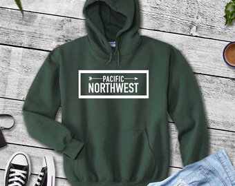 May include: A dark green hooded sweatshirt with a white rectangle on the front that says "PACIFIC NORTHWEST" with an arrow pointing to the right.