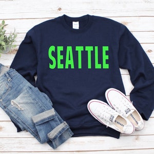 May include: A navy blue sweatshirt with the word "SEATTLE" printed in bright green letters.