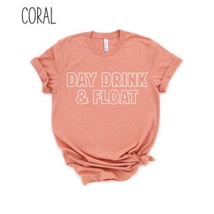 Op de afbeelding: Koraal gekleurd T-shirt met de tekst "DAY DRINK & FLOAT" in witte omrande letters.