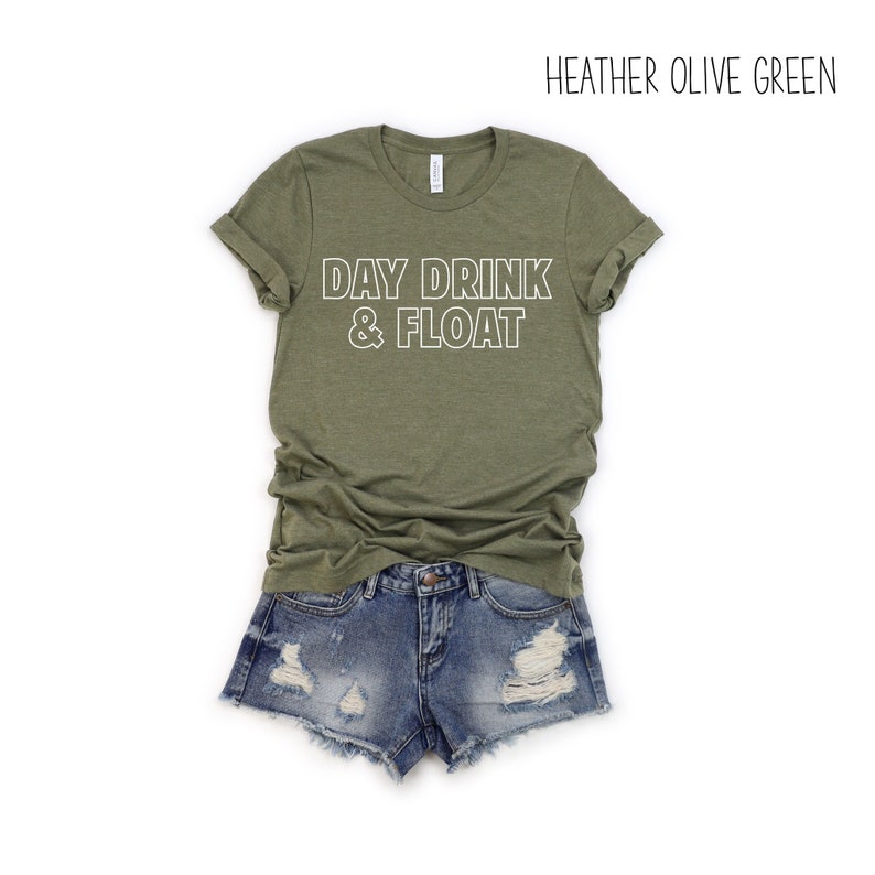 Op de afbeelding: Een heide olijfgroen T-shirt met de tekst "DAY DRINK & FLOAT" in witte omrande letters.