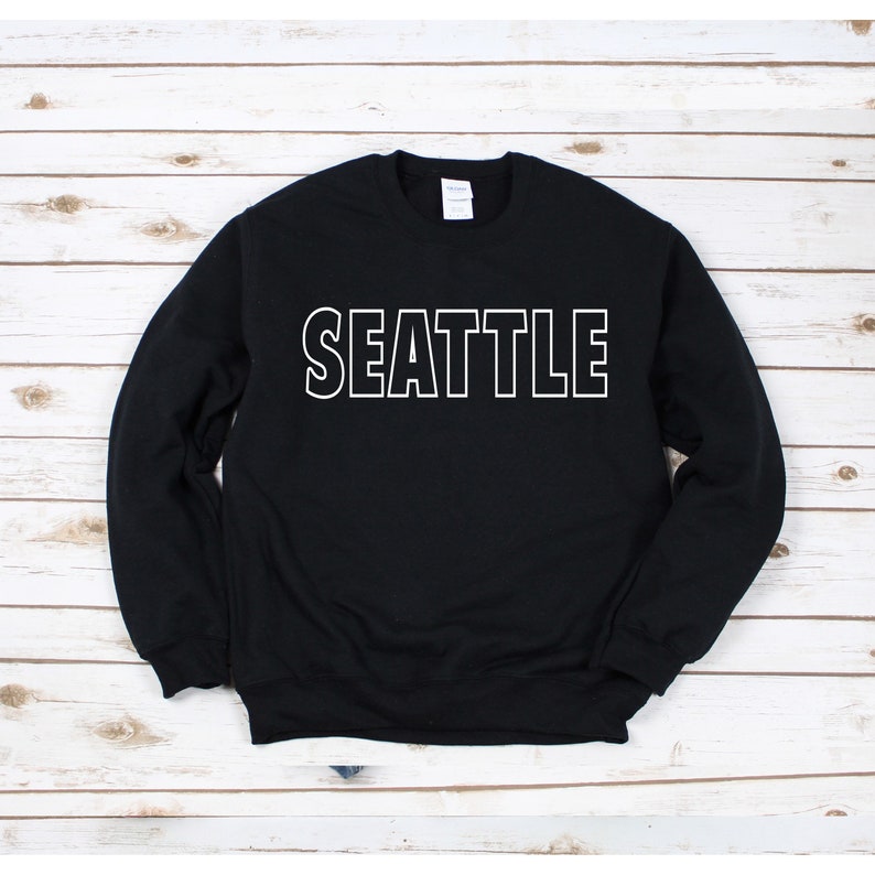 Peut inclure: Sweat-shirt noir avec un texte blanc qui dit "SEATTLE" sur le devant.