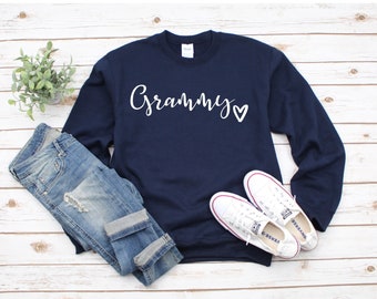 Könnte beinhalten: Navyblauer Sweatshirt mit dem Wort "Grammy" und einem weißen Herz auf der Vorderseite. Der Sweatshirt wird mit einer blauen Jeans und weißen Turnschuhen kombiniert.