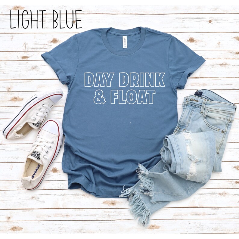 Op de afbeelding: Een lichtblauw T-shirt met de tekst "DAY DRINK & FLOAT" in witte omrande letters.
