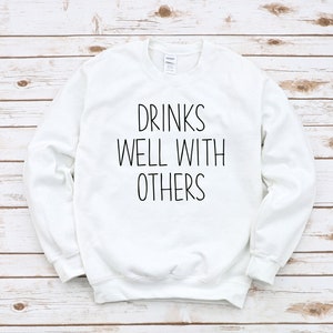 Może przedstawiać: Biała bluza z czarnym napisem "Drinks well with others".