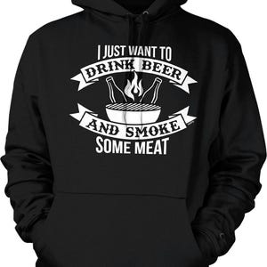 May include: Black hooded sweatshirt with a white graphic. The graphic reads "I JUST WANT TO DRINK BEER AND SMOKE SOME MEAT" with images of beer bottles, a grill, and flames. The sweatshirt has a front pocket.