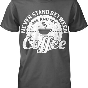 May include: Dark gray t-shirt with a white distressed circle graphic that says "Never stand between me and my coffee". The graphic includes a stylized coffee cup with steam coming from it.